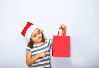 Cute Caucasian kid girl in red Santa's hat holding red paper bag empty copy space for design or text. Banner. Christmas mockup template.