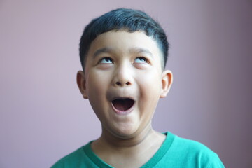 A 6 year old boy wearing a green t-shirt makes a funny face.