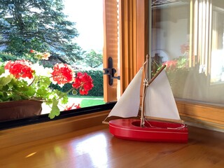 Rotes Spielzeug Segelboot  mit weißen Segeln auf einer Fensterbank aus Holz bei geöffnetem ...