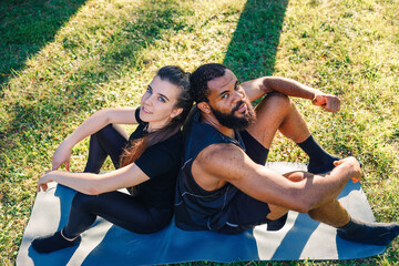 A black boy and a girl playing sports in the garden and standing back to back.