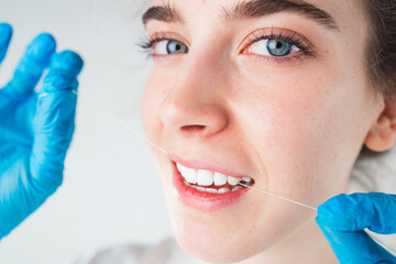 Close-up view young woman on white background, holding dental floss to clean teeth, taking care of...
