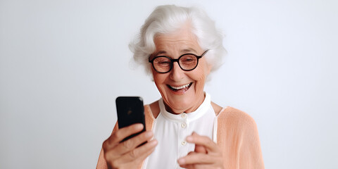 A beautiful elderly woman in glasses on a white background looks at the phone and smiles