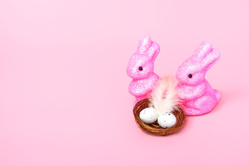 Easter bunnies and a nest with eggs on a pink background. Holiday concept. Closeup copy space