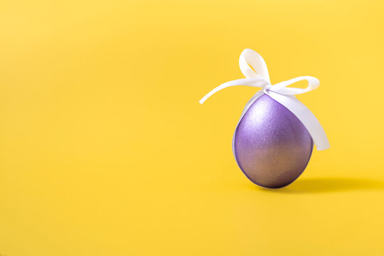 Easter purple egg with a white bow on a yellow background. Closeup copy space.