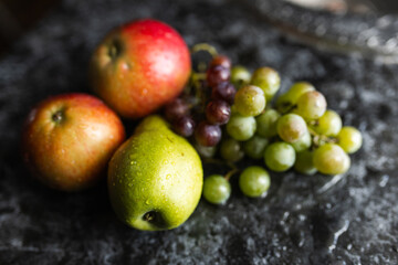 Naklejka na ściany i meble Apples, pears, green and purple grapes lie on a dark background. Organic fruit close-up. Fruits on a black background. Wet washed fruits on a black marble table