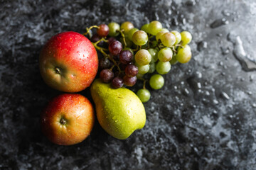 Naklejka na ściany i meble Apples, pears, green and purple grapes lie on a dark background. Organic fruit close-up. Fruits on a black background. Wet washed fruits on a black marble table
