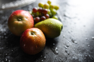 Apples, pears, green and purple grapes lie on a dark background. Organic fruit close-up. Fruits on a black background. Wet washed fruits on a black marble table