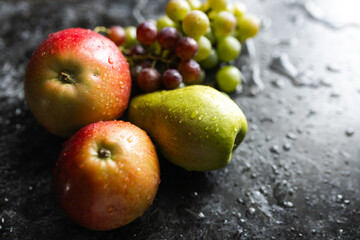 Apples, pears, green and purple grapes lie on a dark background. Organic fruit close-up. Fruits on a black background. Wet washed fruits on a black marble table