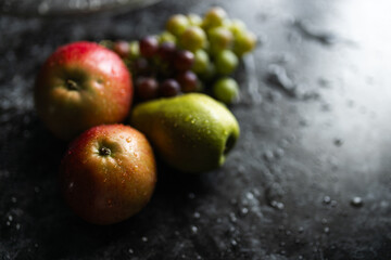 Apples, pears, green and purple grapes lie on a dark background. Organic fruit close-up. Fruits on a black background. Wet washed fruits on a black marble table