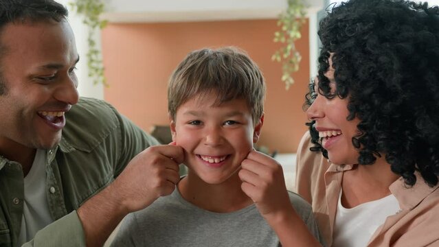 Multiracial family portrait loving African American parents father mother pinching cheeks of smiling little boy kid junior schoolboy happy mom and dad love cute child affectionate relationship at home