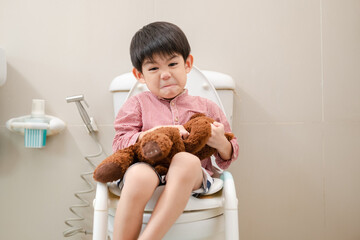 Asian boy Sitting on the toilet bowl in hand holding teddy bear