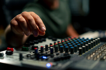 A close-up of a mixing console device used by a man working as professional sound engineer in a music studio