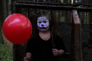 Serious girl in spooky outfit stylized as Pennywise looking at camera while standing in abandoned...