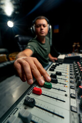 Concentrated male sound engineer working at the mixing console in a music studio to record a...