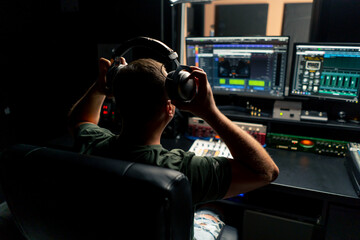 a male sound engineer sits at a mixing desk with his back to camera and puts on headphones