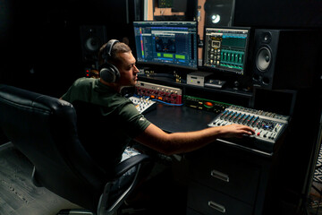 a focused male sound engineer wearing headphones sits at a mixing desk recording new track
