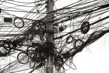 A jumble of electrical and telephone wires attached to a pole in Bangkok, Thailand.
