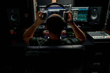 a male sound engineer sits at a mixing desk with his back to camera and puts on headphones