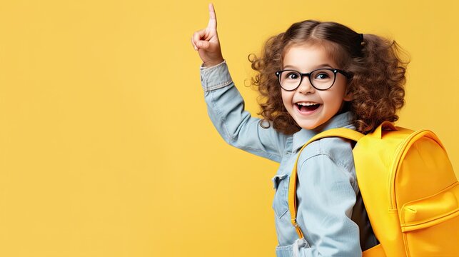 Joyful girl with glasses pointing up, wearing a yellow backpack.
