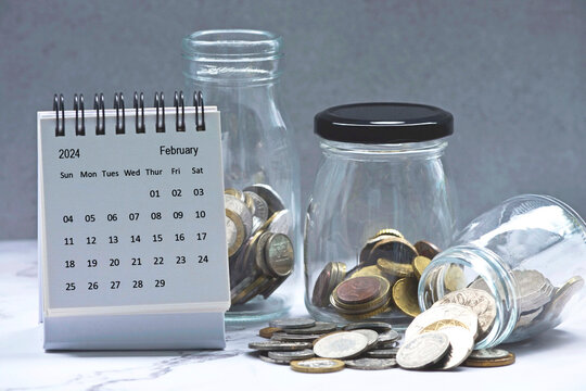 February 2024 calendar and glass jars with multicurrency coins.