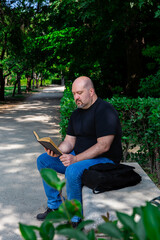 Obraz premium 45-50 year old bald man concentrating on reading a book sitting on an outdoor park bench on a sunny afternoon
