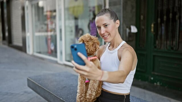 Young caucasian woman with dog taking selfie photo with smartphone sitting on bench at street