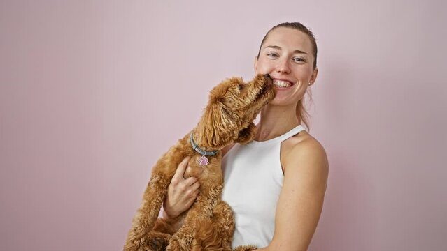Young caucasian woman with dog smiling kissing over isolated pink background