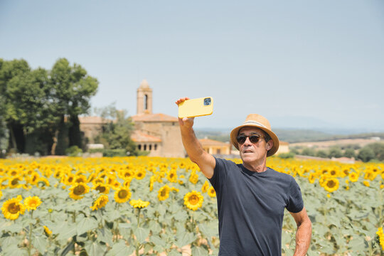 Elderly man with hat and sunglasses takes selfie on holiday, sunflower field in the background. Elderly man arriving at his holiday resort in Pubol, Girona.