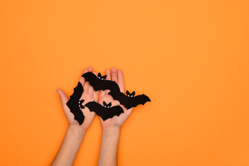 Halloween decorations black bats in the hands of a child on an orange background. Halloween concept. Halloween card