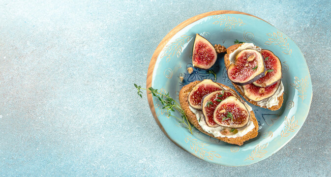 Figs and soft white cheese on toasted rye bread on a blue background, Long banner format. top view
