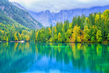 Laghi di Fusine inferior lake, Tarvisio, Italy. Amazing autumn landscape, crystal clear water with reflection and colored forest surrounded by Mangart mountain range, outdoor travel background