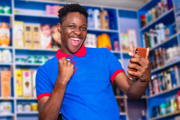 image of excited young salesman with mobile phone isolated over a shopping mall and celebrating