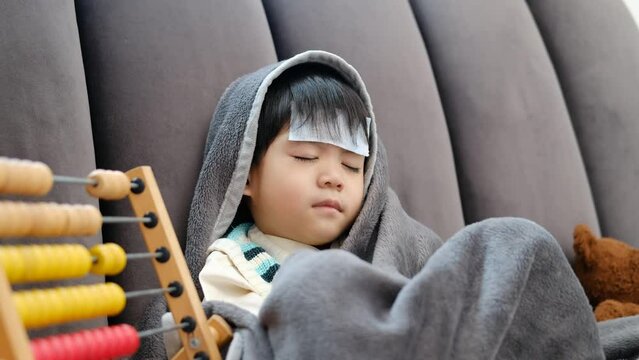  Asian boy Lying sick, he had a fever reducing patch on his forehead and covered himself with a blanket because of the cold.