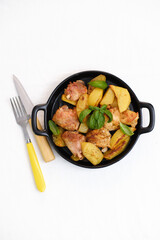 Fried chicken and potatoes on black plate on white background.