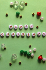 Various beads with Merry Christmas caption on green background. Top view.