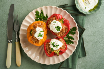 Roast stuffed red and yellow bell peppers with couscous, brown rice and spelled with Greek sauce and olive oil on rustic wooden background. Healthy dinner eating. Autumn cozy dinner concept. Top view