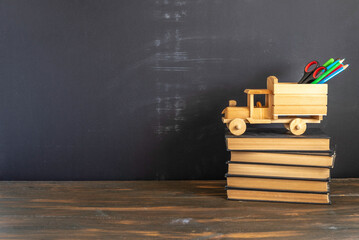 A stack of books, truck-shaped pencil holder in front of blackboard background. Free space for...