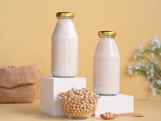 Organic soy milk in glass bottle on white podium and soybean in bowl on beige background. vegan product, Minimalist concept and Healthy drinks
