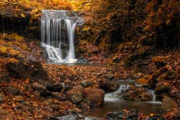 Beautiful waterfall in the autumn forest with fallen leaves on the rocks