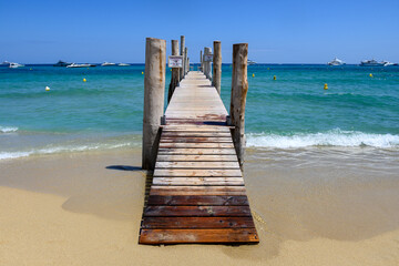 Wooden pier and crystal clear blue water of legendary Pampelonne beach near Saint-Tropez, summer vacation on French Riviera, France, text translation: it's dangerous not to dive from pier.
