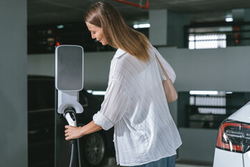 Young woman travel with EV electric car to shopping center parking lot charging in downtown city...