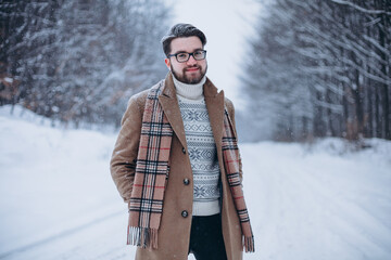 Attractive stylish young man in glasses walking in winter park