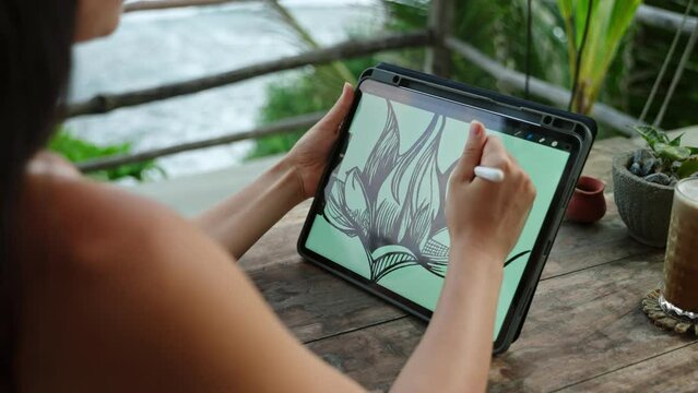 Female illustrator hands draw on tablet at cafe with ocean view, palm trees. Freelancer working outdoor on the terrace at the seaside. Pretty woman drink cappuccino. Close-up, back view.