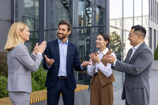 Business people outside office building applauding and congratulating colleague boss with promotion and good results achievement, four people, women and men on work break outdoors.