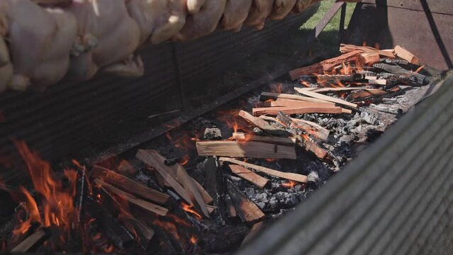 Fire wood in cooking barbecue pit rotating slowly in slow motion above flames to heat and warm roasted chicken, roast beef, hot dogs, and other raw meat in a tasty smoked format