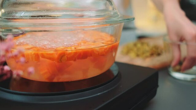 Boiling finely chopped carrots in a glass saucepan on an electric stove. Close-up of the table. Cooking in the kitchen