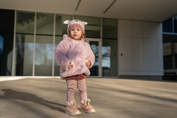 Fototapeta premium Small caucasian girl toddler stand in front of building in winter day