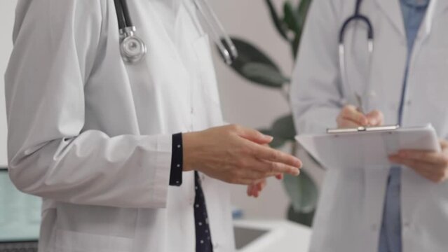 Two female doctors are using a clipboard and medical notes while standing and discussing health treatment in a hospital. Medicine concept
