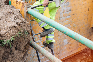 Groundworker builder using steps ladder to get out of the deep drainage eaxcavation trench support box. Builder going up using ladder. Safe workplace fall prevention concept