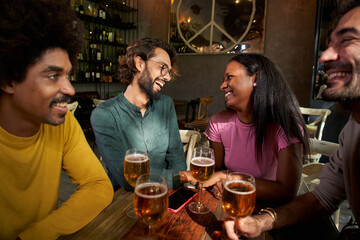 Group of young friends having beer in a bar and smiling. This four multi-ethnic friends are smiling and having fun.